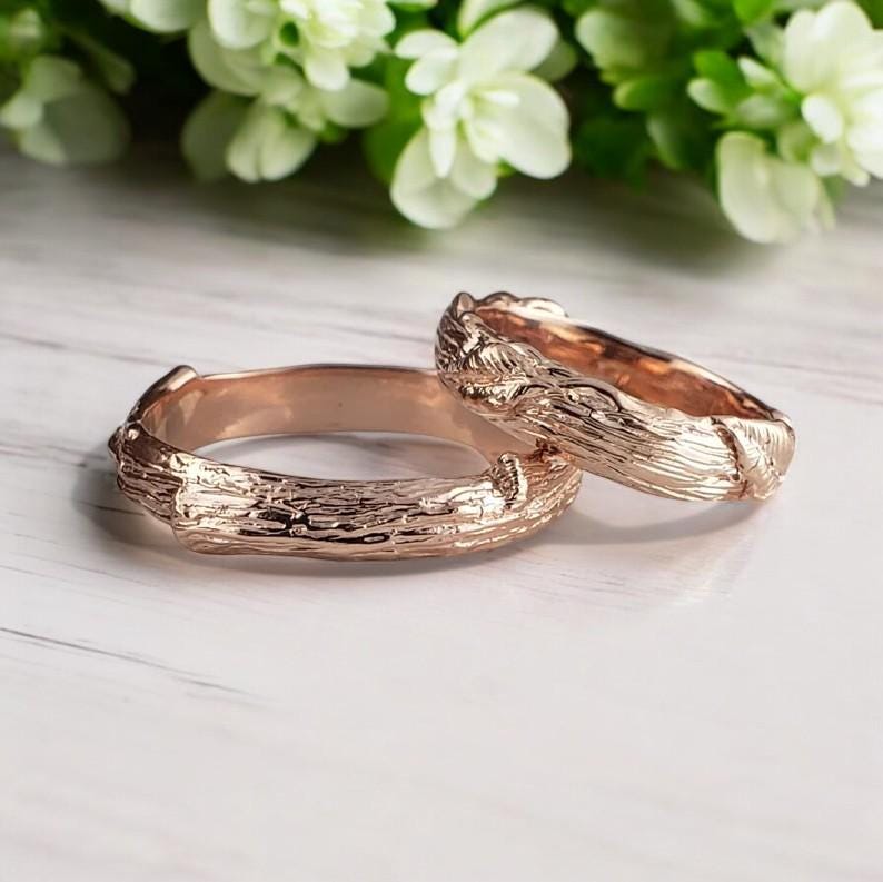 2 wedding bands with tree bark texture with hand-sculpted leaves on one of the rings, shown in solid rose gold