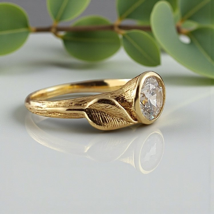 Gold ring with a diamond on a reflective surface with green leaves in the background
