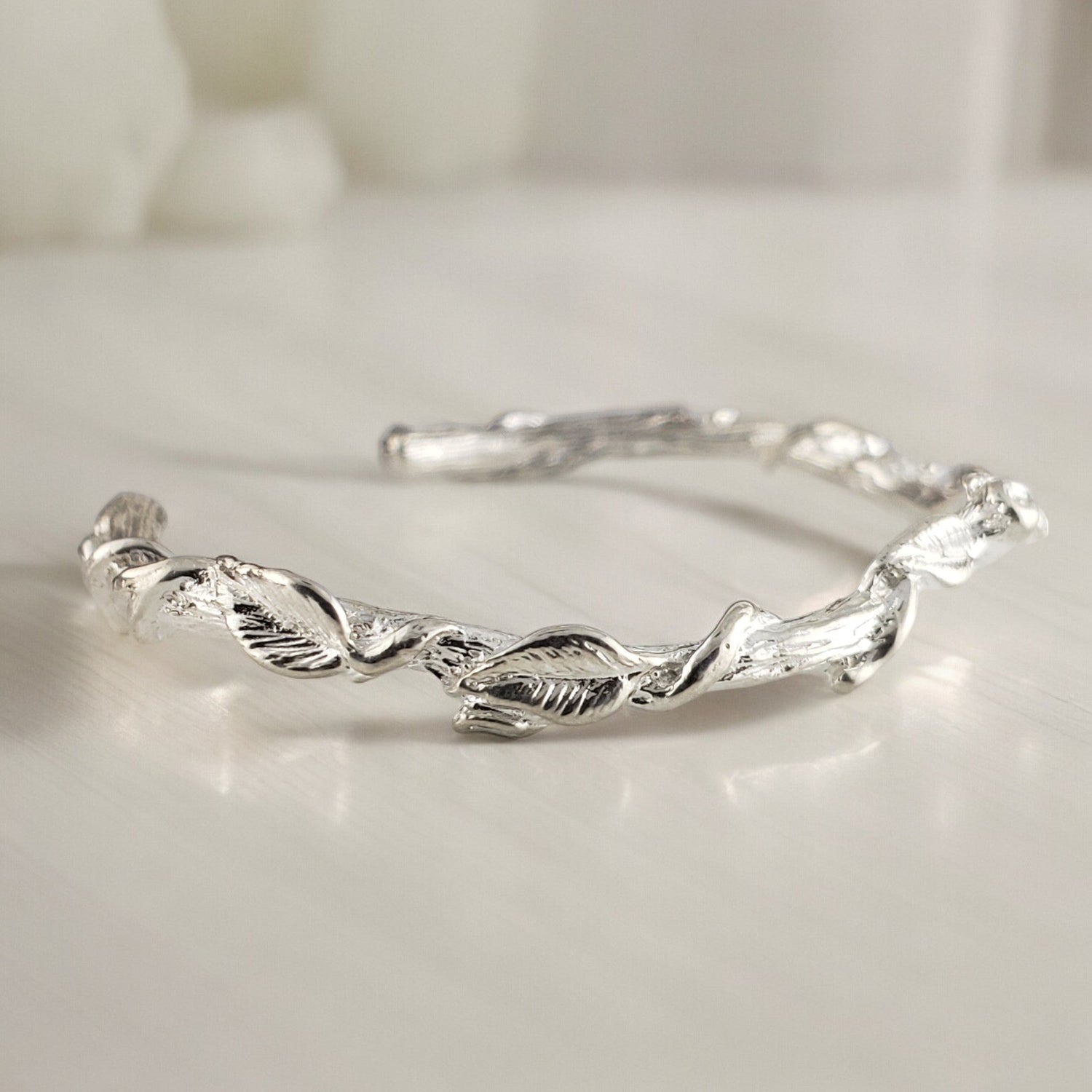 white gold and silver cuff bracelet on a table with tiny leaves all around the design