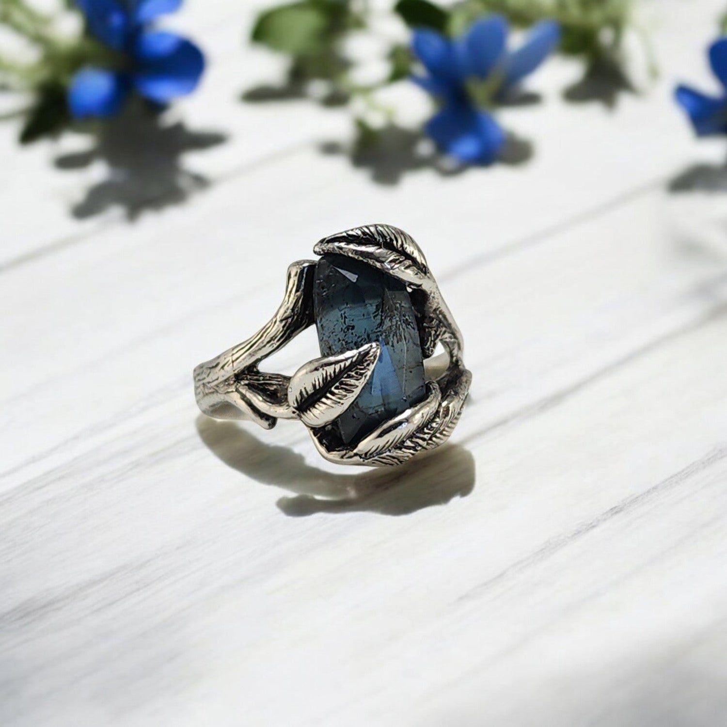 teal blue moss kyanite stone with leaves draped around the stone in this silver ring setting