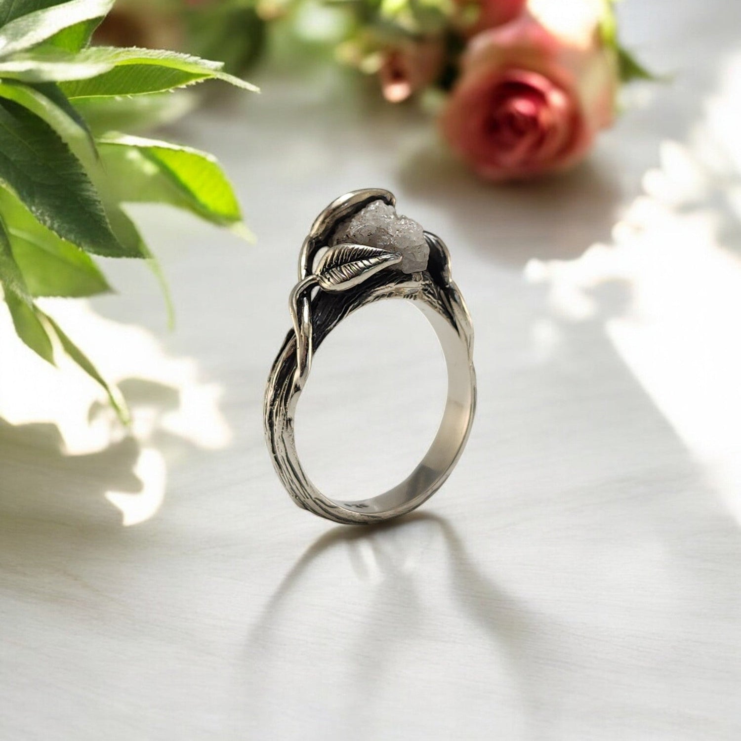 raw diamond ring in silver with leaves draped over the stone