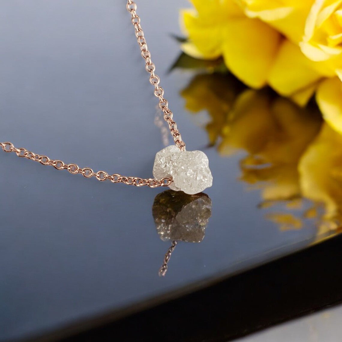 raw diamond with a yellow chain going through the center of it laying on a mirrored table