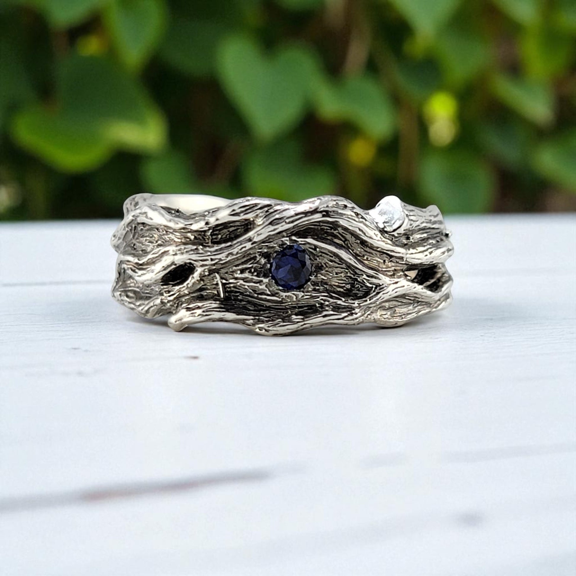 sterling silver ring with a wood texture featuring a small blue sapphire