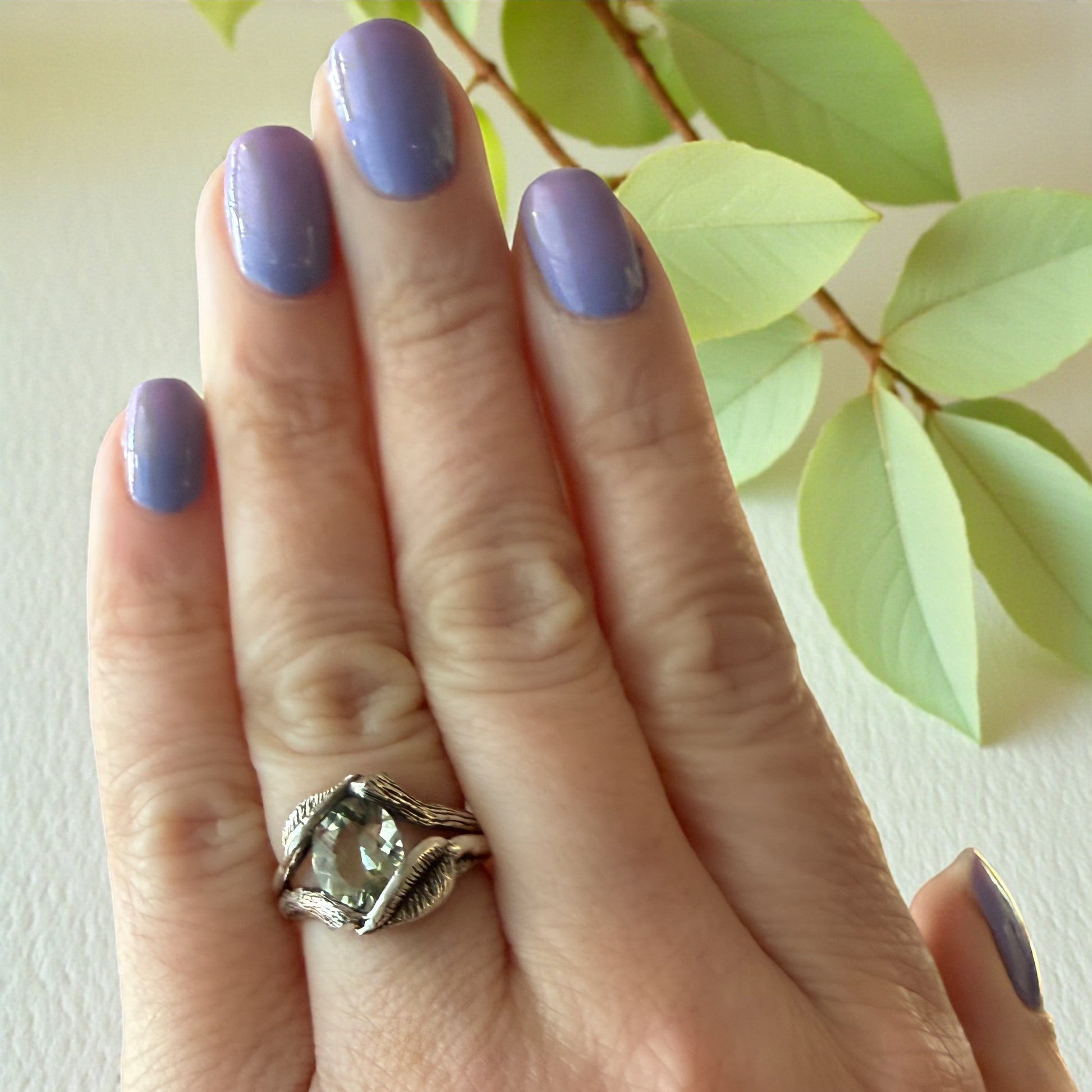 shiny green amethyst gemstone ring in sterling silver on a hand with leaves wrapped around the stone
