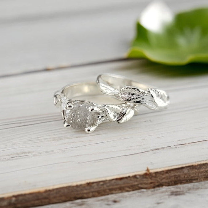Silver ring with leaf design with a raw white diamond on a wooden surface