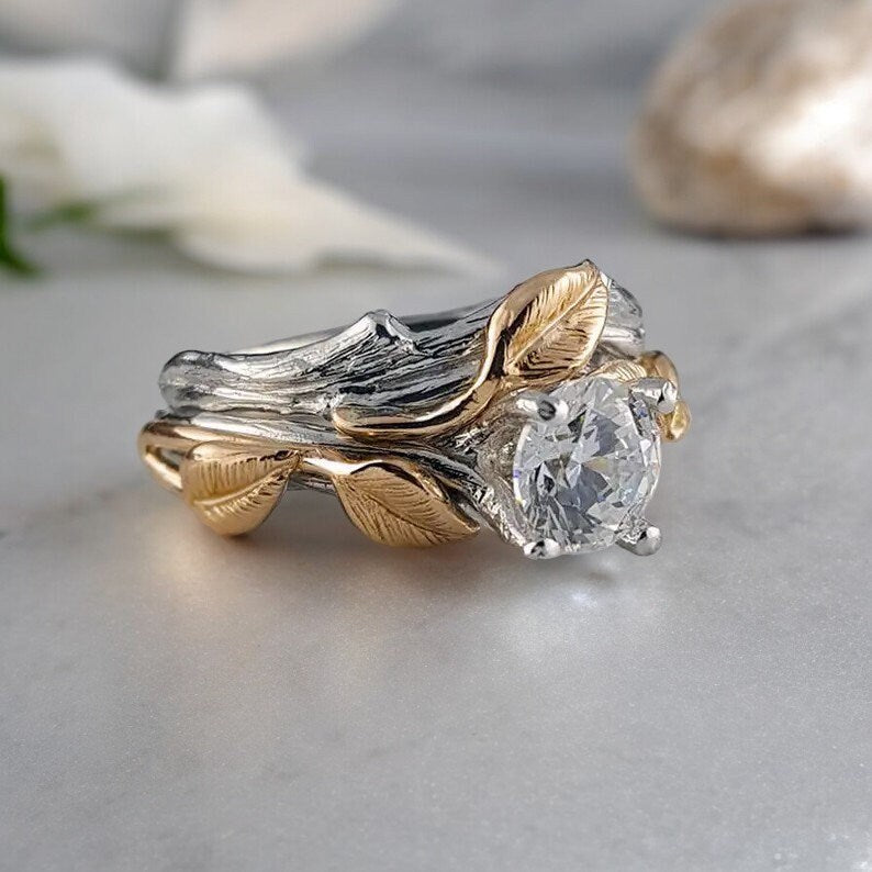 Gold and silver leaf-themed ring with a diamond on a light gray surface.