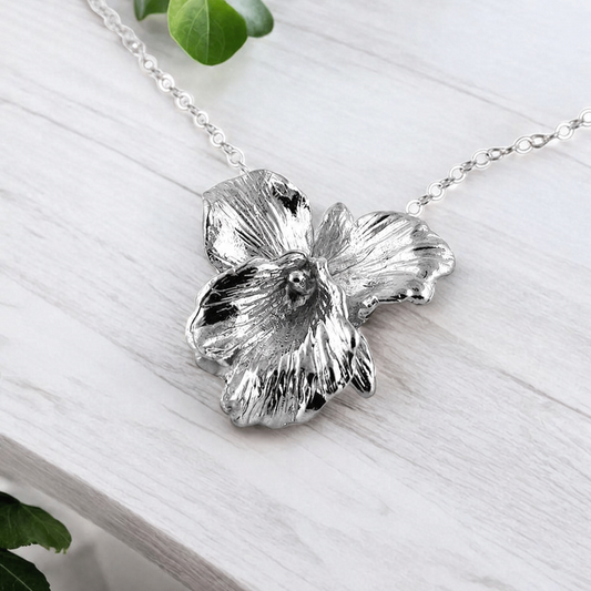 Silver flower-shaped pendant on a chain against a light wooden background