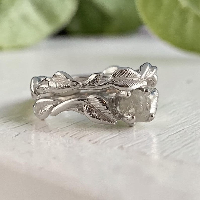 Silver leaf-patterned ring on a light surface with green leaves in the background