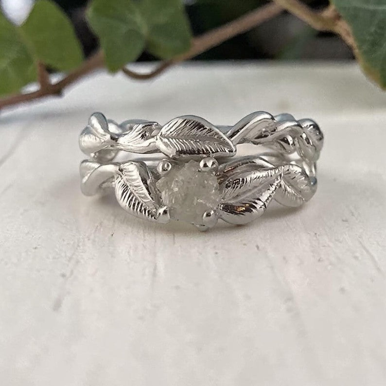 Silver leaf-patterned ring on a light surface with green leaves in the background
