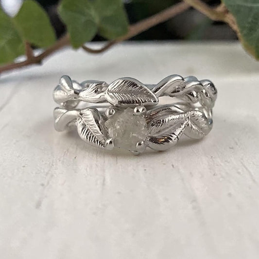 Silver leaf-patterned ring on a light surface with green leaves in the background