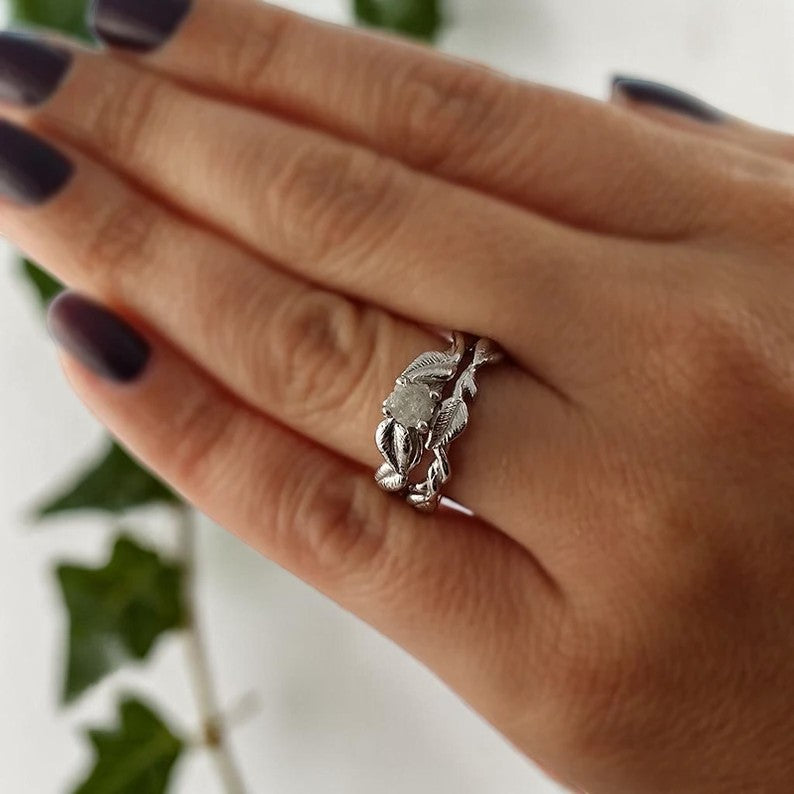 Silver leaf-shaped ring on a person's finger with a blurred green plant background