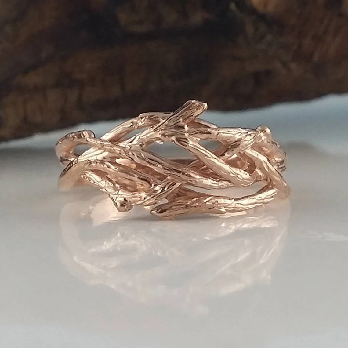 Rose gold branch-like ring on a white surface with a blurred brown background